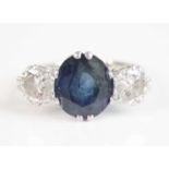 A white metal, sapphire and diamond three stone ring, featuring a centre oval faceted sapphire