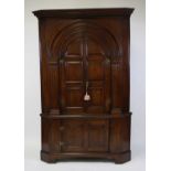 A George III oak corner cupboard in two sections, having a Greek Key moulded cornice above an arched