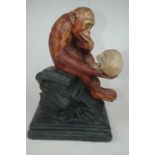 A painted plaster figure of a monkey with a skull in his hand, seated upon some books and