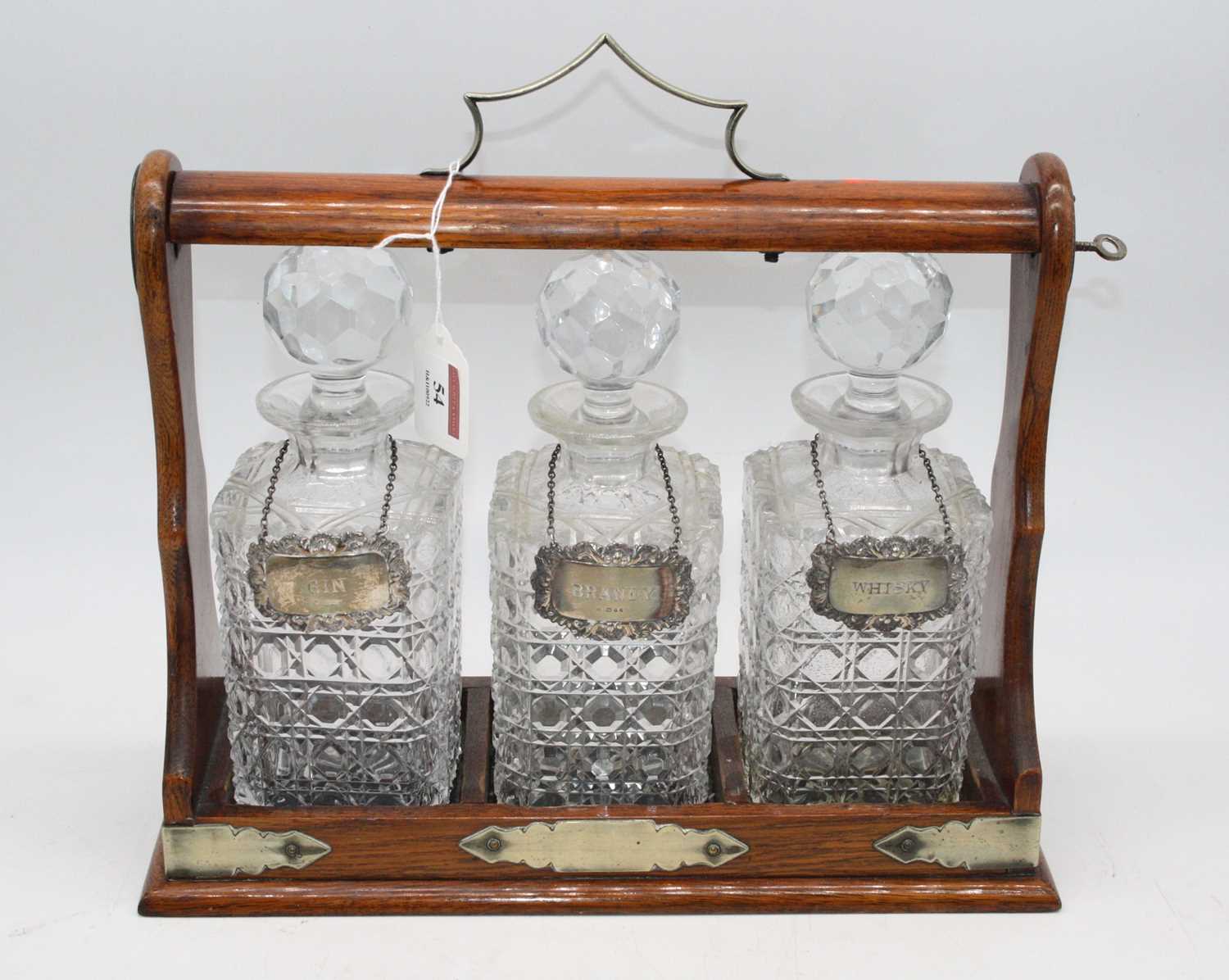 An oak cased three decanter tantalus, w.34cm, each decanter bearing a silver label, inscribed for