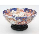 A Japanese export porcelain bowl, decorated with exotic birds and flowers, upon a carved hardwood
