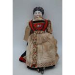 A continental porcelain headed doll, having fabric body and in orginal native dress, 30cm