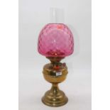 An early 20th century brass pedestal oil lamp having cranberry tinted glass shade