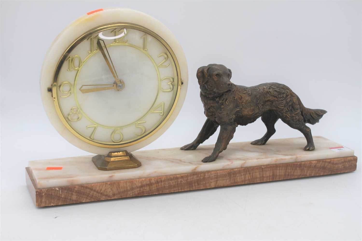 An Art Deco polished hardstone mantel clock, surmounted by a spelter model of a dog, w.50cm