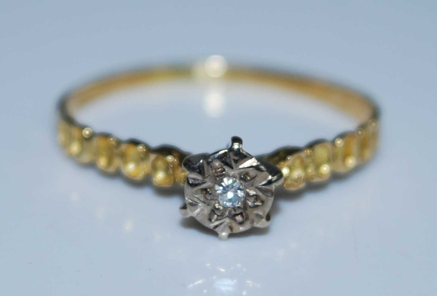 A yellow and white metal diamond single stone ring featuring a round brilliant cut diamond in an