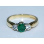 An 18ct yellow and white gold, emerald and diamond three stone ring, featuring a centre oval emerald