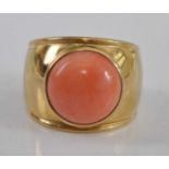 A yellow metal coral dress ring, comprising a 13mm round pink coral cabochon bezel set within a wide