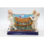 A reproduction majolica style table centrepiece, the central bowl supported by four cherubs with