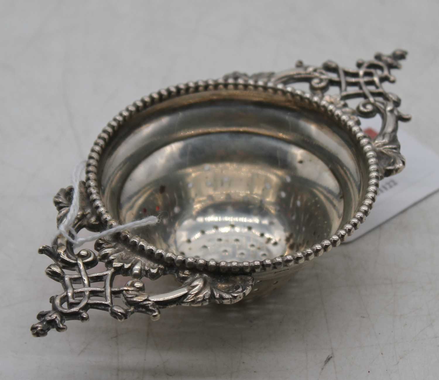 A George V silver tea strainer, having pierced scrolling handles within reeded border, 1.7oz
