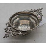 A George V silver tea strainer, having pierced scrolling handles within reeded border, 1.7oz