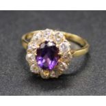 An 18ct gold, amethyst and diamond cluster ring, arranged as a central oval cut claw set amethyst