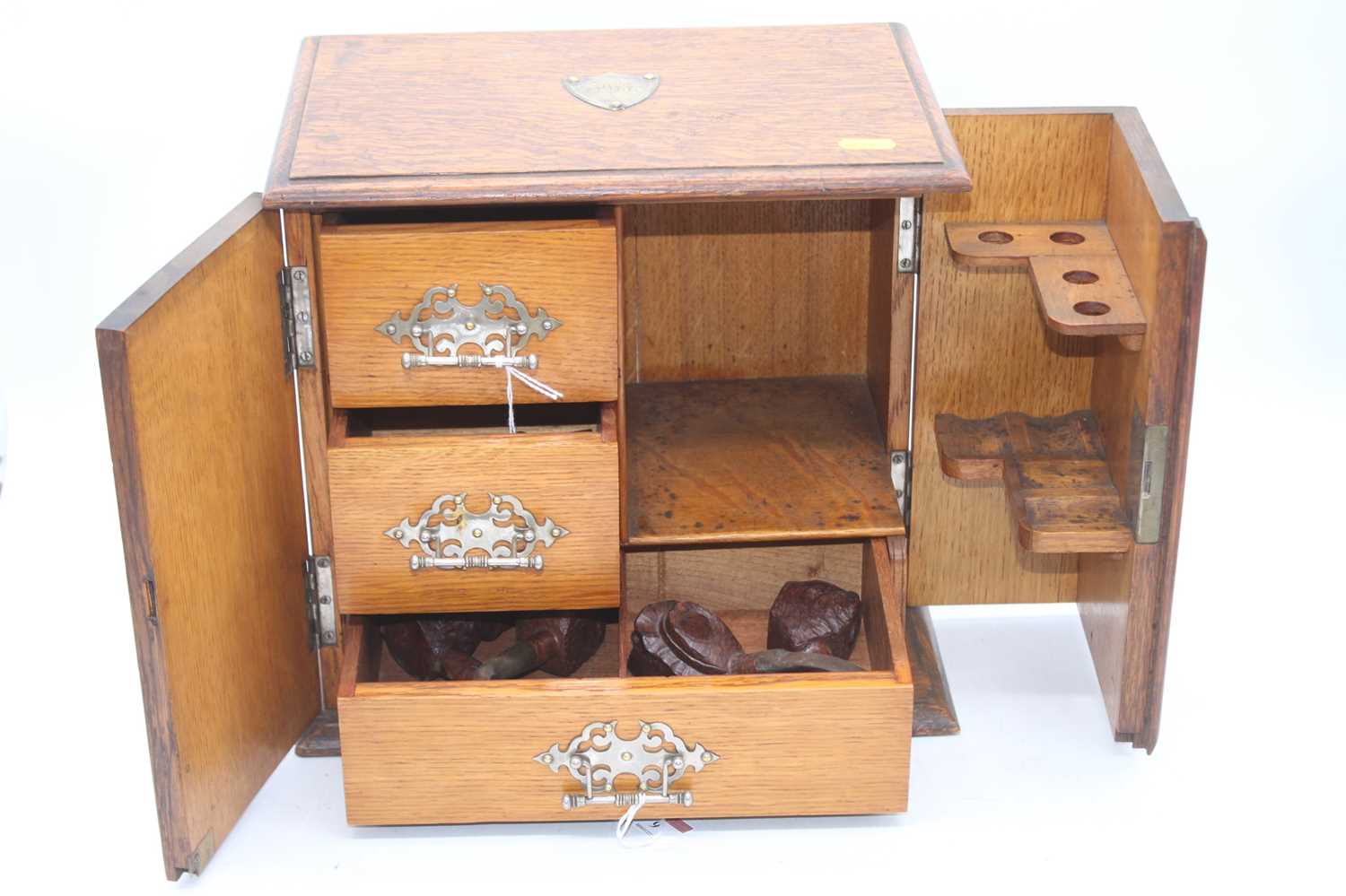 An early 20th century oak smoker's cabinet, the doors opening to reveal a pipe rack and drawers,