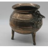 A 17th century bronze tripod cauldron, having iron swing handle, each leg decorated with a mask,