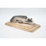 A bisque porcelain model of a recumbent greyhound, mounted upon a polished hardstone plinth, w.27cm