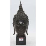 A bronze buddha head, mounted upon a polished black hardstone plinth, height 32cm