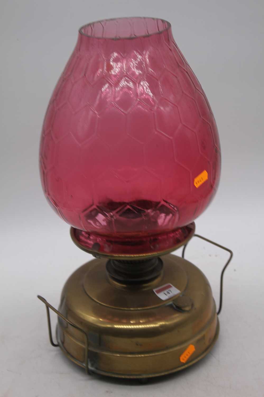 A Victorian brass oil lamp, the large cranberry tinted glass shade above a plain brass font,