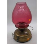 A Victorian brass oil lamp, the large cranberry tinted glass shade above a plain brass font,