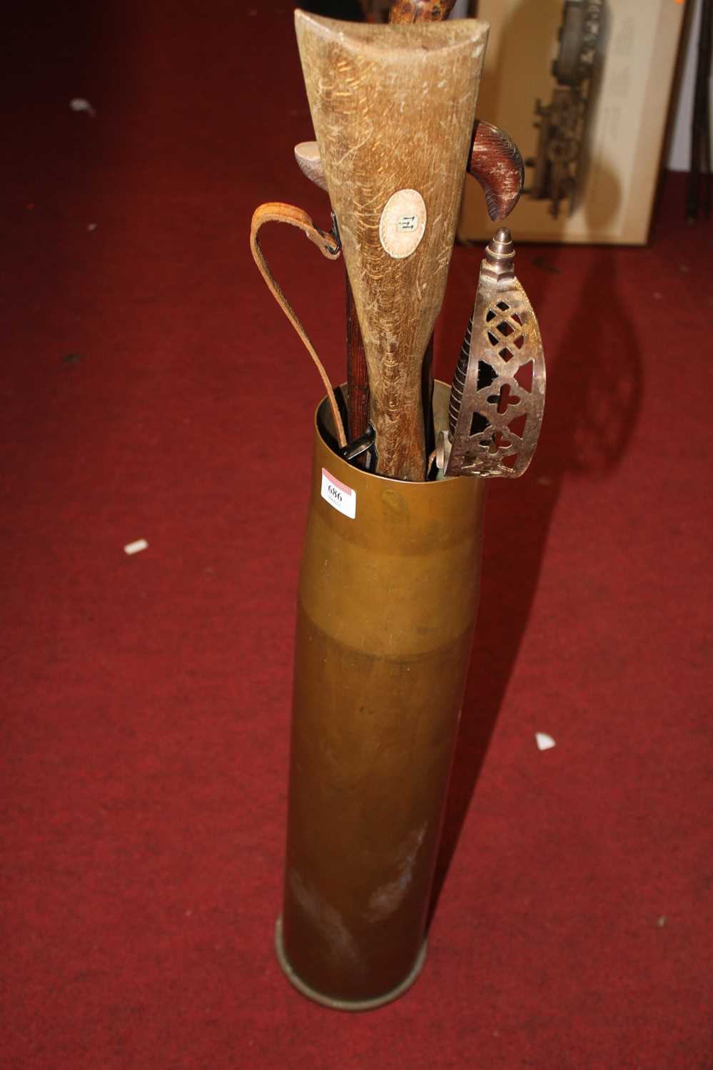 A brass artillery shell case, containing a knife-sharpener, air rifle model, and two walking sticks