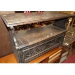 An early 20th century ebonised and floral relief carved oak fold-over monks bench, having typical