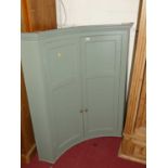 A contemporary painted double door corner cupboard of concave form