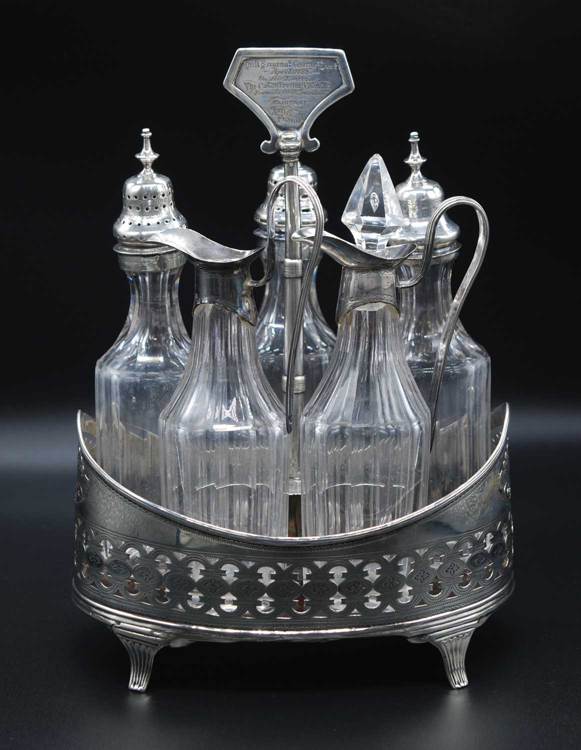 A George III white metal five bottle cruet stand, of pierced oval form with mahogany base, the