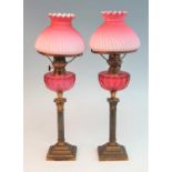 A pair of Victorian brass oil lamps, the wrythen pink silk glass shades above a cranberry glass font