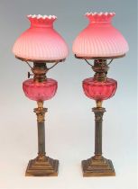 A pair of Victorian brass oil lamps, the wrythen pink silk glass shades above a cranberry glass font