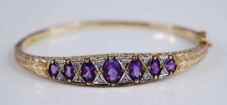 A 9ct gold, amethyst and diamond hinged bangle, arranged as seven graduated oval cut amethysts,