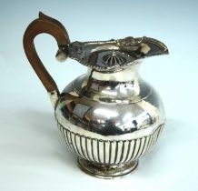 A late Victorian silver hot water jug, of half-reeded bellied form with hinged cover, wooden