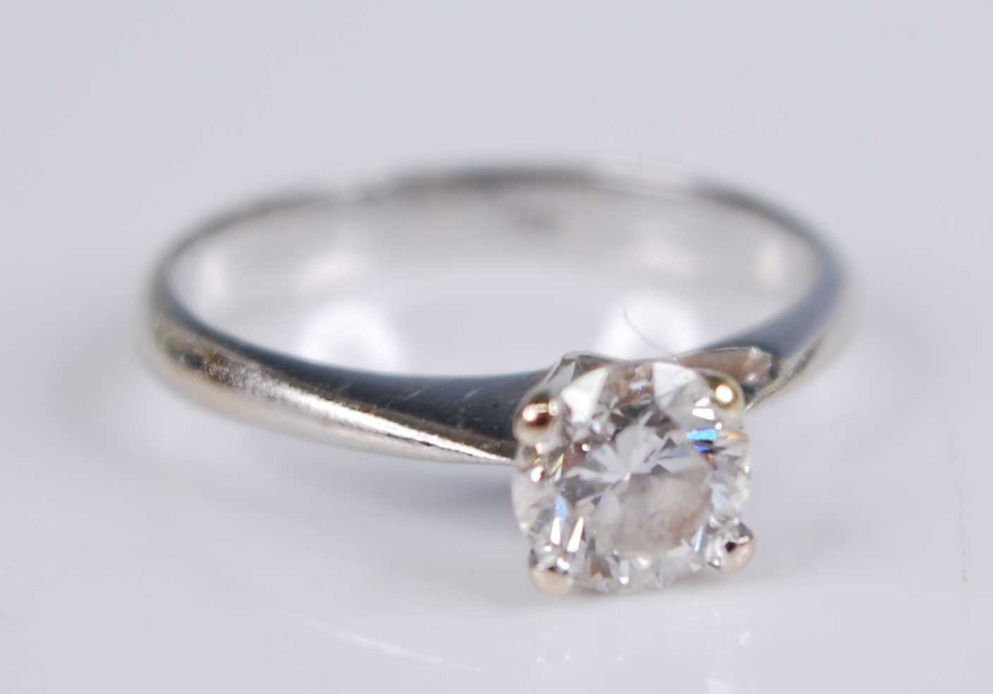 A white metal diamond solitaire ring, with a round brilliant cut diamond in a four-claw V shaped