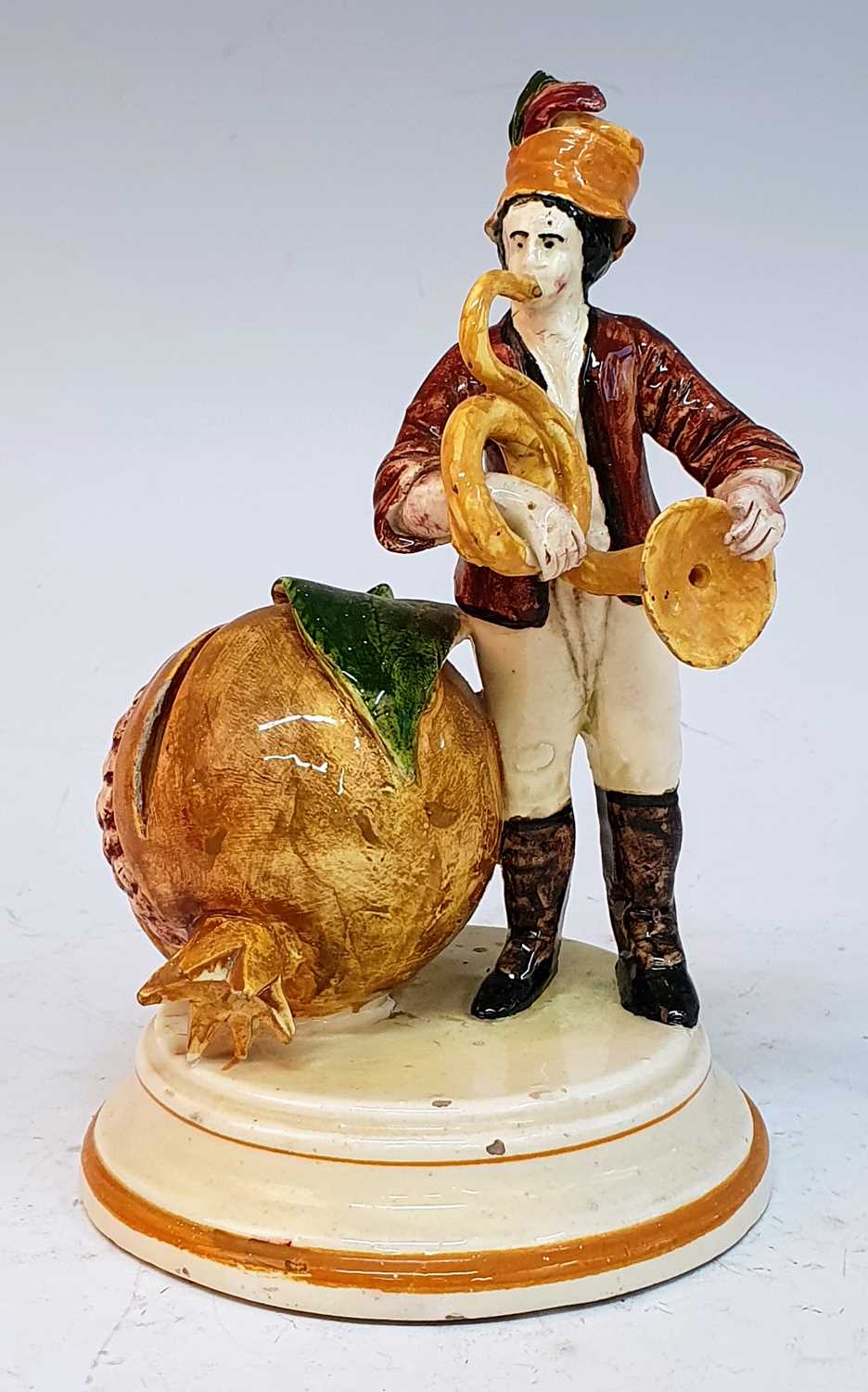 A 19th century continental cream glazed earthenware moneybox, in the form of a man playing a horn