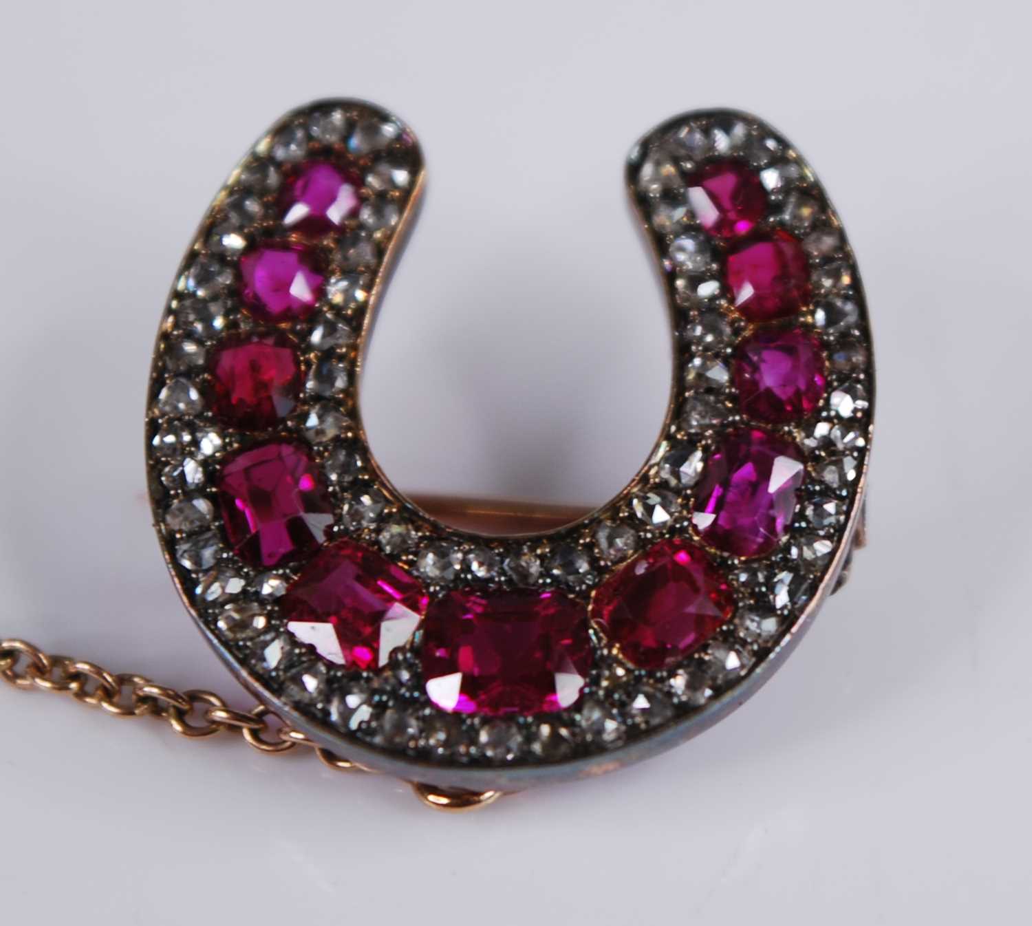 A late Victorian yellow metal, ruby and diamond horseshoe brooch, featuring eleven graduated oval