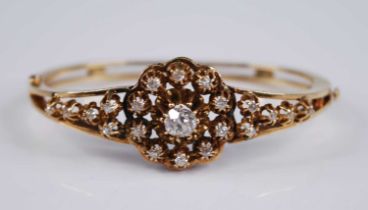 A yellow metal diamond set hinged bangle, the Edwardian style flower head openwork setting