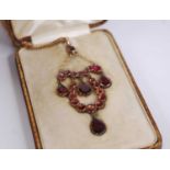 An Edwardian yellow metal and garnet set pendant of horseshoe outline, arranged as pear and round
