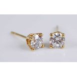 A pair of yellow metal diamond single stone stud earrings, each featuring a round brilliant cut