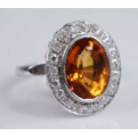 A platinum citrine and diamond oval cluster ring, comprising a centre oval faceted citrine within