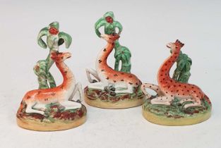 A collection of three circa 1860 Staffordshire models of giraffes, each shown resting beneath a palm