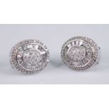 A pair of 18ct white gold diamond oval cluster earrings, each featuring a centre panel of 19 melee