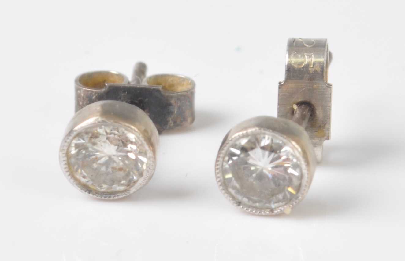 A pair of white metal diamond stud earrings, each comprising a round brilliant cut diamond in a
