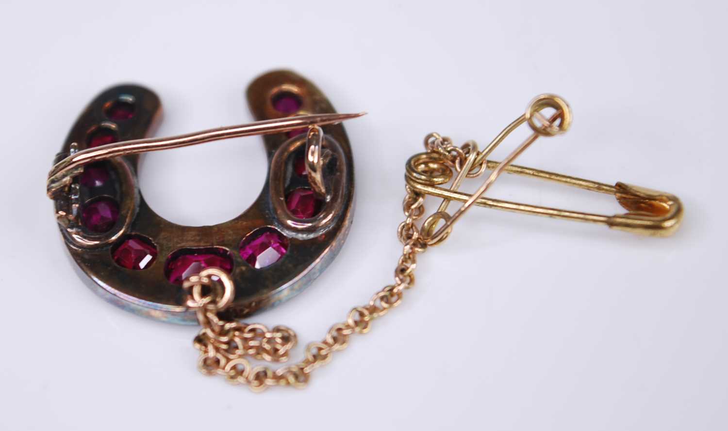 A late Victorian yellow metal, ruby and diamond horseshoe brooch, featuring eleven graduated oval - Image 2 of 2