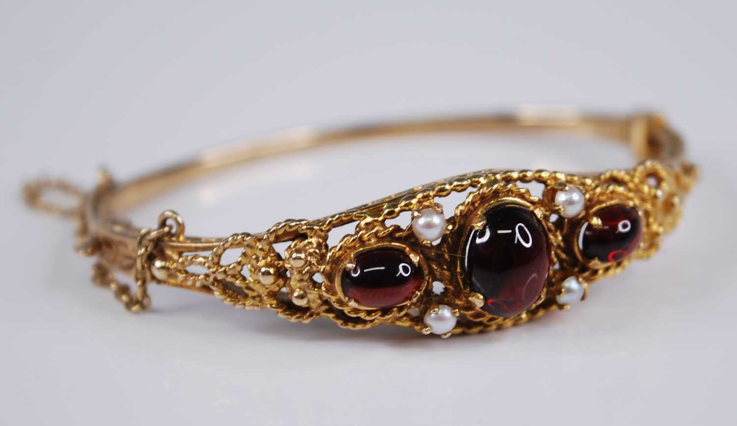 A Victorian style 9ct gold, garnet and seed pearl hinged bangle, the three cabochon garnets