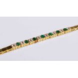 A contemporary yellow metal, emerald and diamond bracelet, arranged as seven oval cut emeralds in
