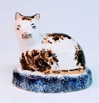 A circa 1860 Staffordshire model of a cat, sponge decorated in ochre and brown upon a cobalt plinth,