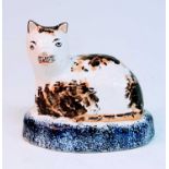 A circa 1860 Staffordshire model of a cat, sponge decorated in ochre and brown upon a cobalt plinth,