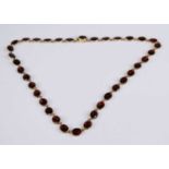 A yellow metal garnet necklet, comprising 36 oval faceted garnets in cut-down grain closed back