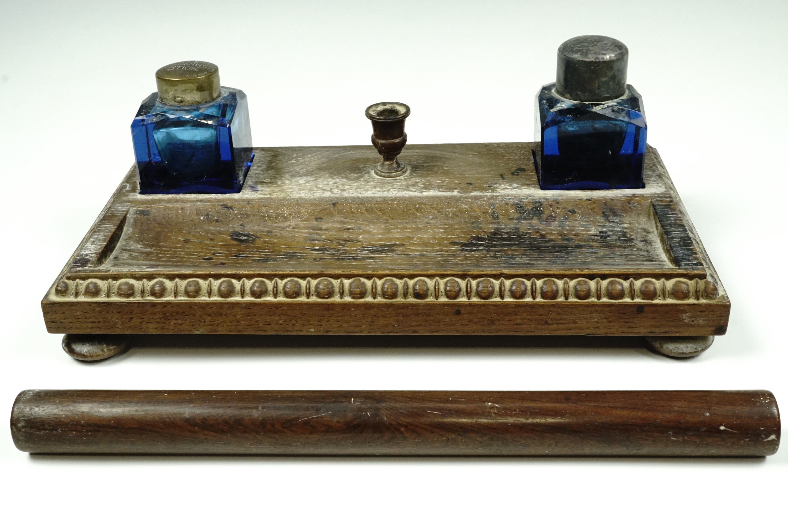 An Edwardian oak ink standish, carrying a pair of facet-cut blue glass ink wells, one having a