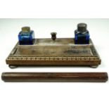 An Edwardian oak ink standish, carrying a pair of facet-cut blue glass ink wells, one having a