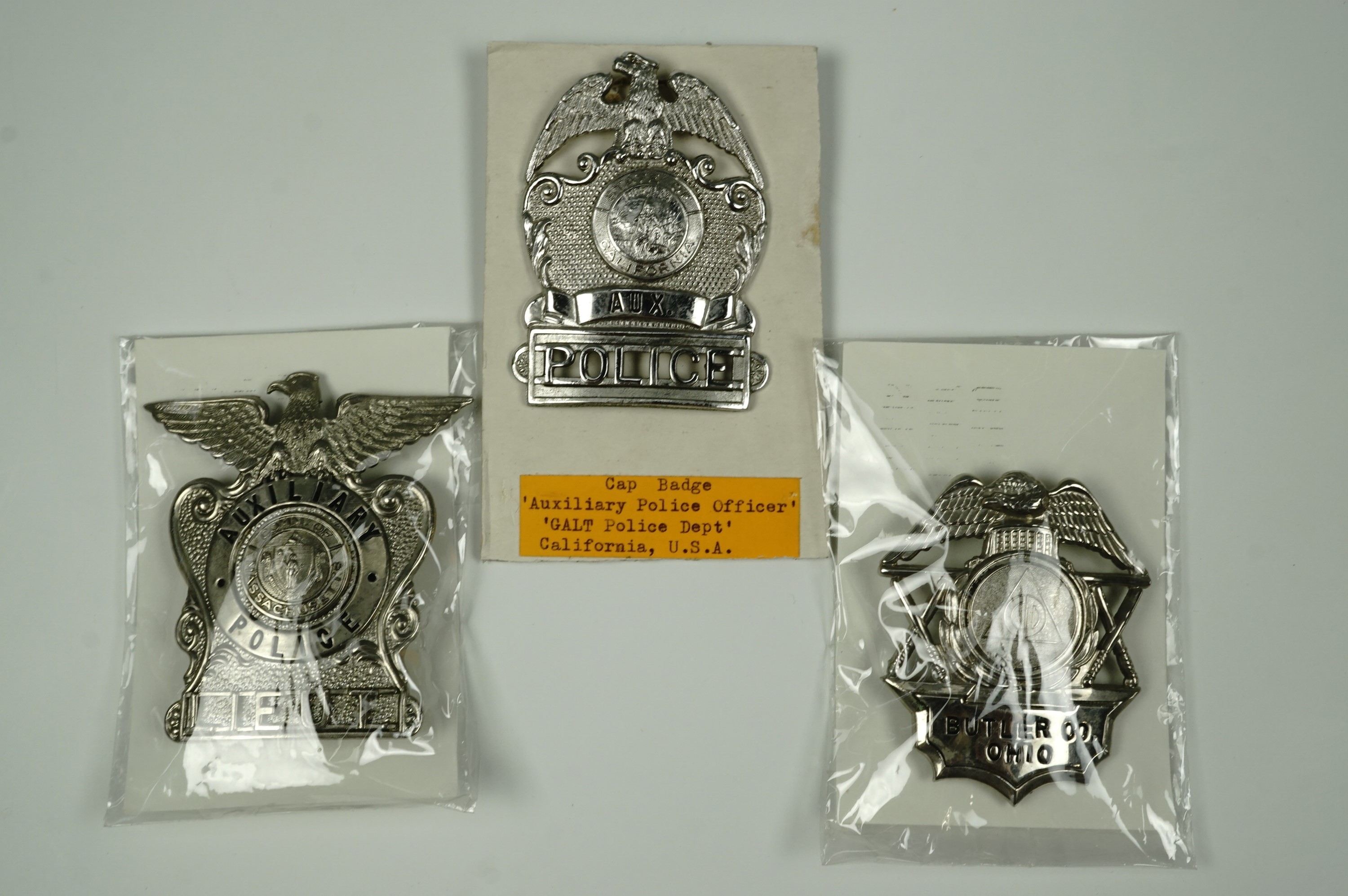 Three American police cap badges, comprising Massachusetts Aux. Police Lieutenant, California Aux.