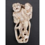 A Japanese ivory netsuke of an Oni carrying a child, 7 cm