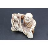 A Japanese ivory netsuke of a man opening a scroll with a child inside, 4 cm